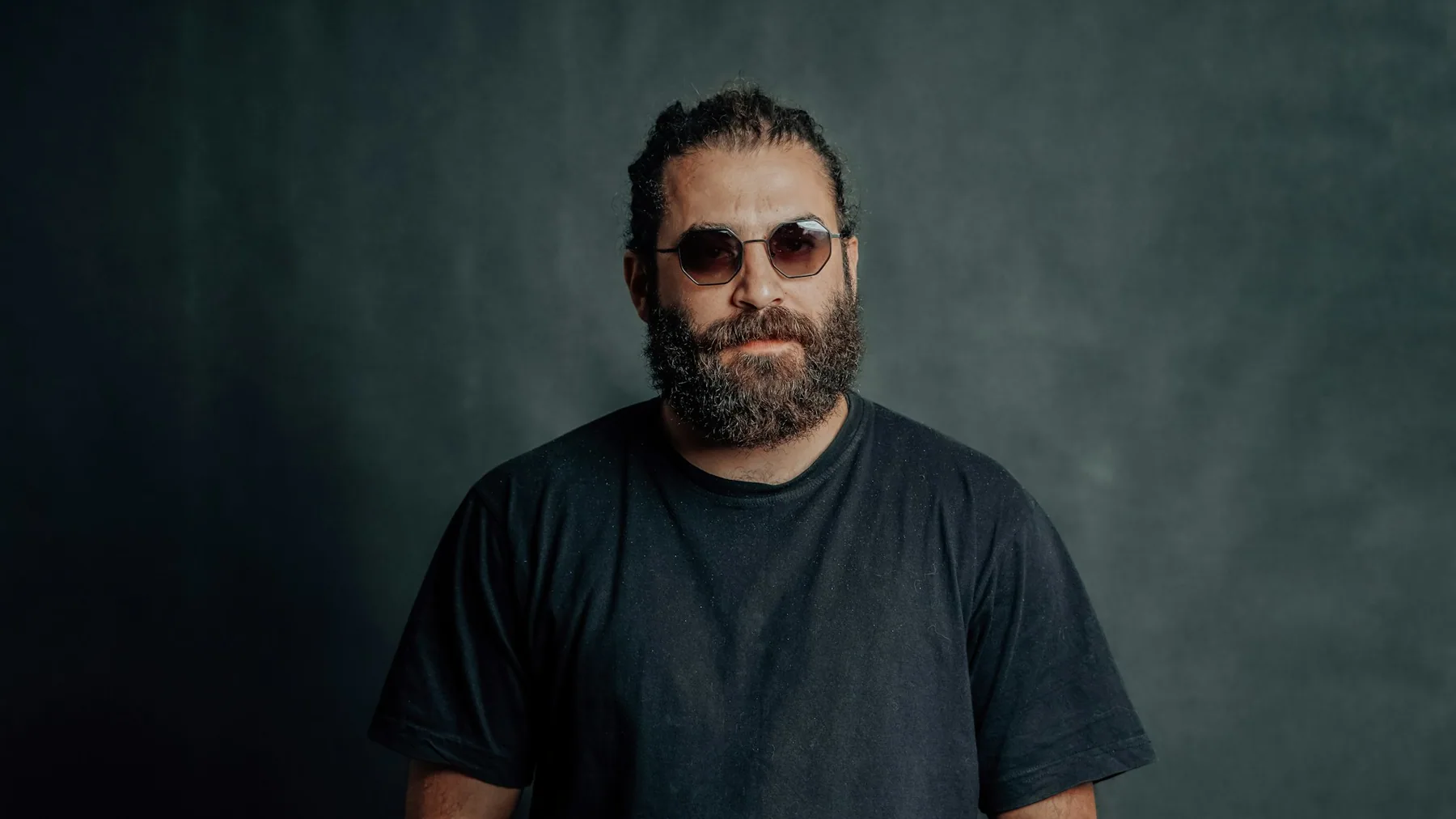 Man in a plain dark t-shirt photographed against a dark background