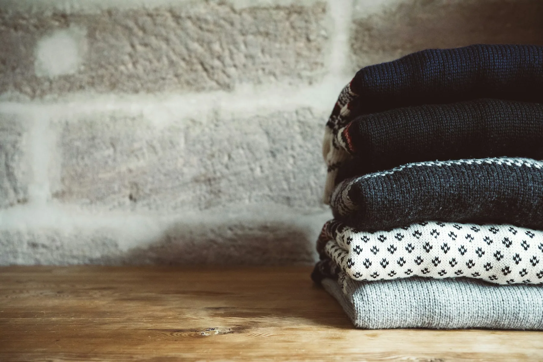 A stack of folded knitwear against a bare wall
