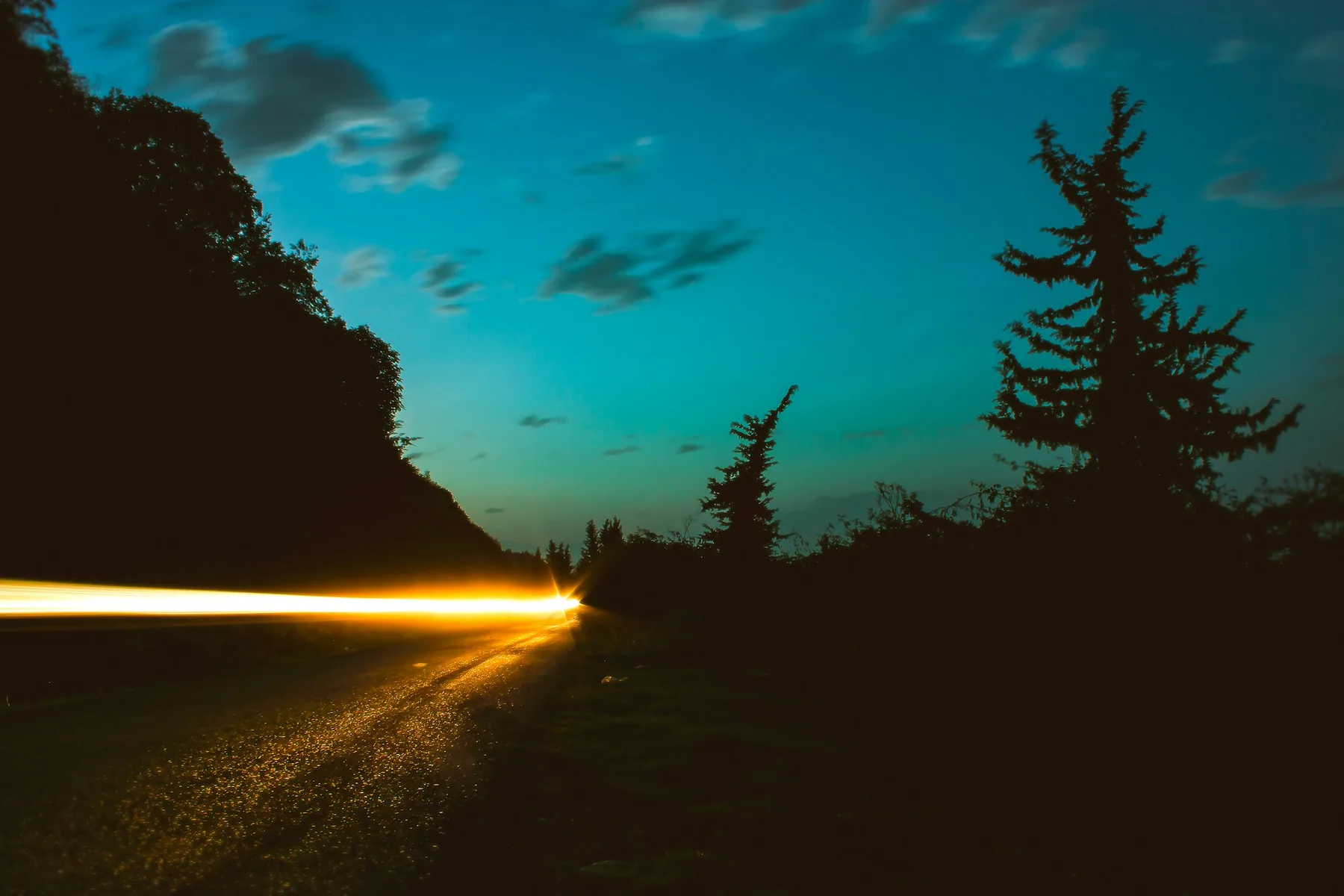 A dark road at dusk with a headlight trail