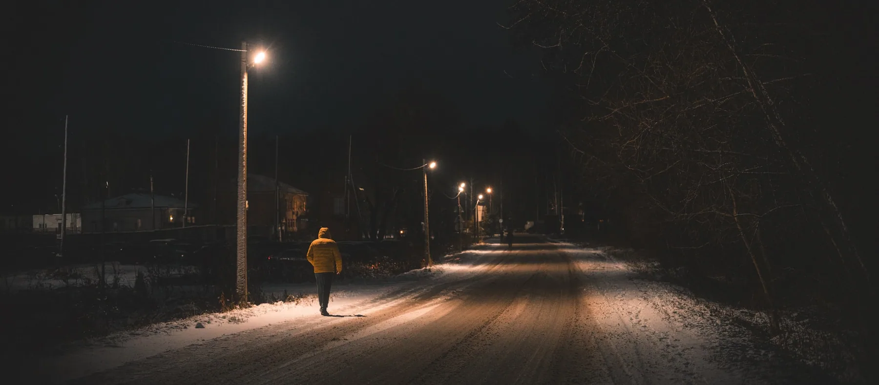A figure in a bright jacket on a lit road at night
