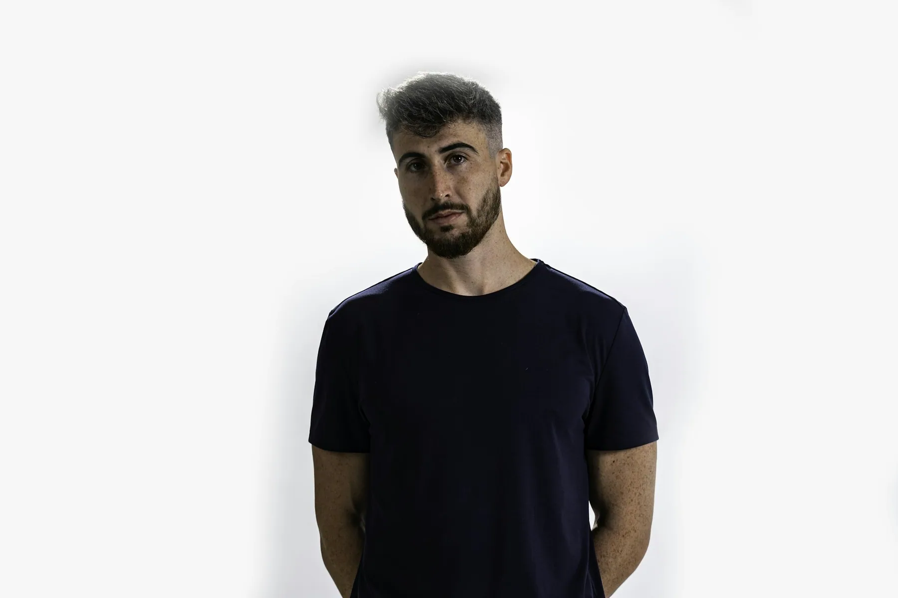 Plain black t-shirt shown on a standing figure against a pale wall